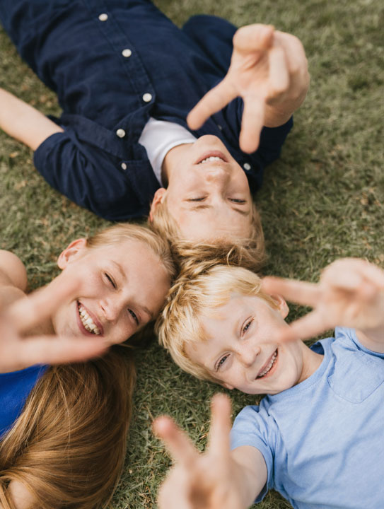 Drei Geschwister liegen auf einer Wiese